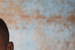 Excited little African boy with hopeful eyes, raised eyebrows and an uneasy smile on his face looking at his pediatrician who is going to inject an intramuscular solution into his arm
