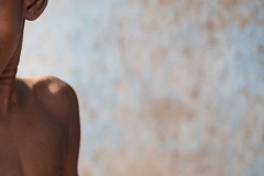 Excited little African boy with hopeful eyes, raised eyebrows and an uneasy smile on his face looking at his pediatrician who is going to inject an intramuscular solution into his arm